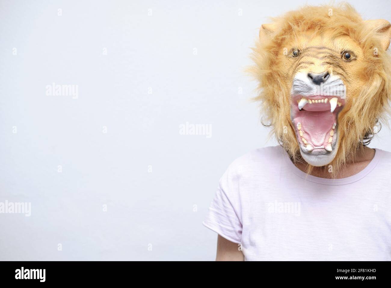 Une femelle dans un masque de lion en colère posant près d'un mur blanc Banque D'Images