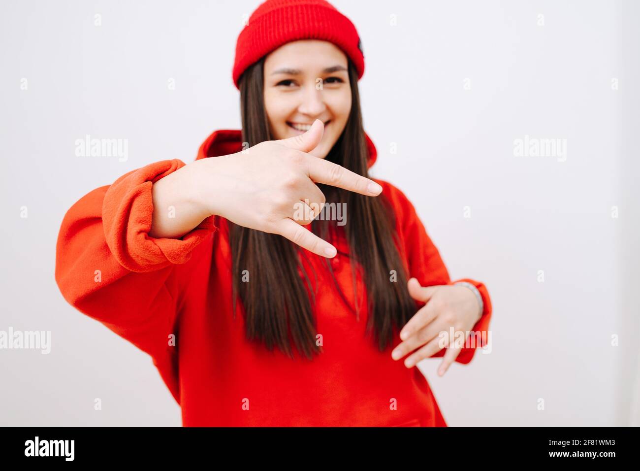 Jeune femme sociale en forme de casquette rouge vif et de sweat à capuche faisant un geste rock'n roll. Elle a de longs cheveux droits sur les côtés. À l'intérieur, devant la wh Banque D'Images