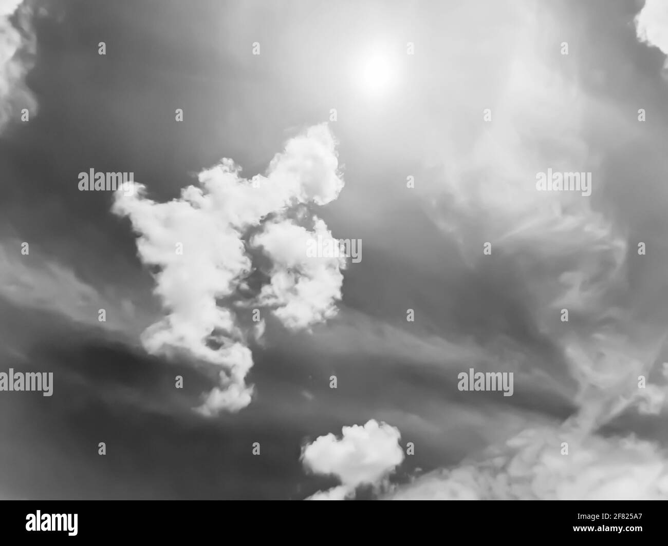 Arrière-plan en forme de nuage plein format avec formes de nuage blanches distinctives et ciel gris blanc contre plein soleil, en noir et blanc monochrome. Banque D'Images