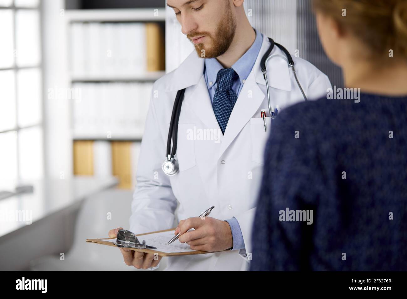 Médecin sympathique à barbe rouge et patiente discutant de l'examen de  santé actuel assis à la clinique Photo Stock - Alamy