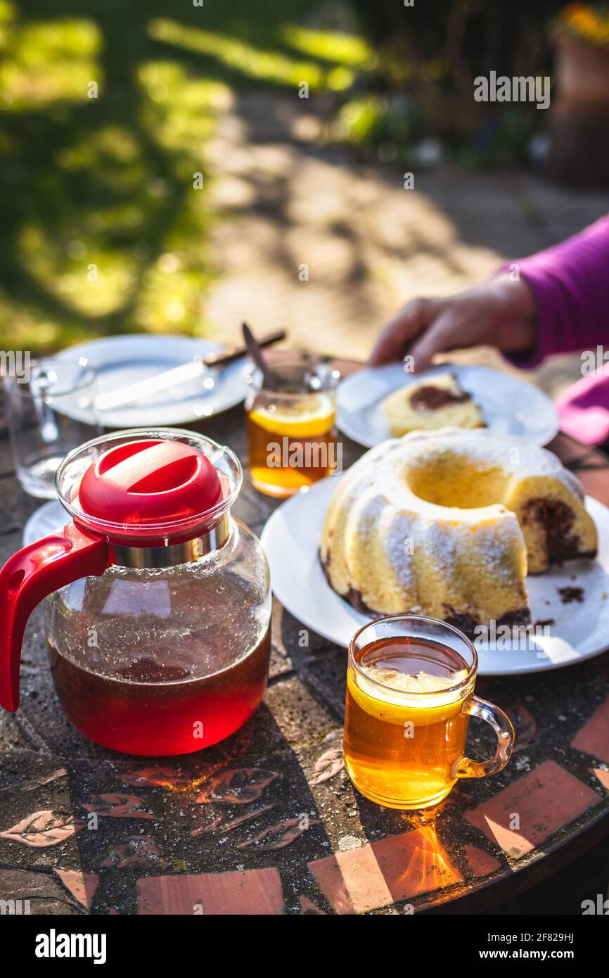 Thé dans une tasse et théière avec gâteau de petit pain sur la table. Dessert et boisson chaude servis dans le jardin de printemps Banque D'Images