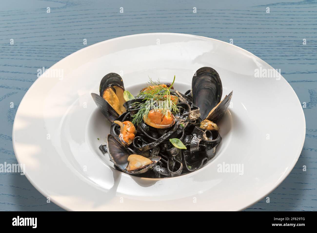 encre calmar de pâtes noires avec moules - tagliatelle italienne al nero di seppia - dans un plat blanc sur bleu table en bois Banque D'Images
