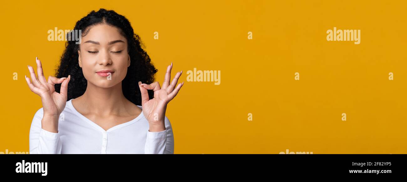 Zen. Jeune femme afro-américaine détendue méditant avec des yeux fermés, fond jaune Banque D'Images