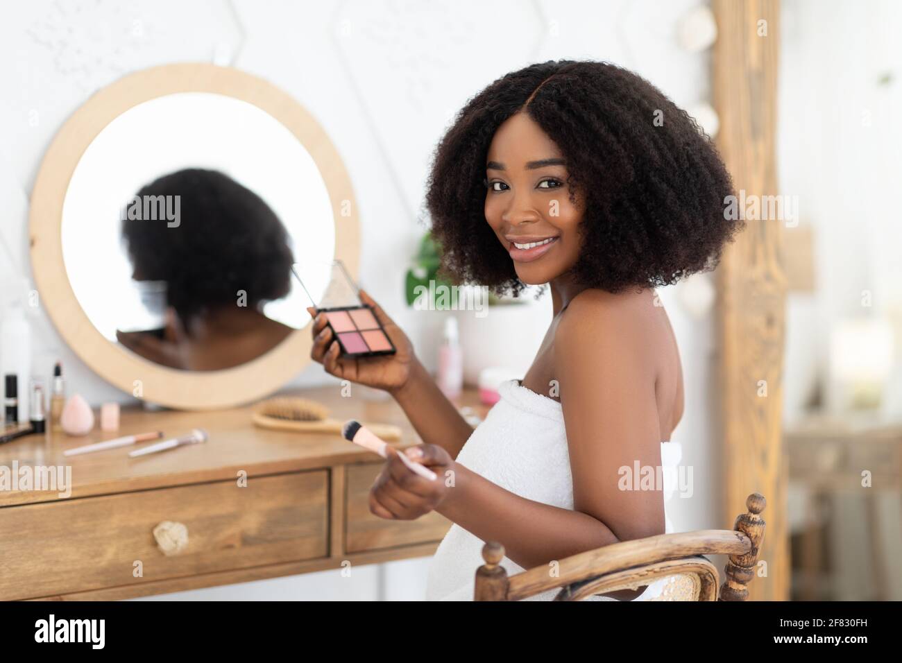 Femme noire appliquant le maquillage devant le miroir, assise à la coiffeuse  avec une palette d'ombres à paupières, souriante à l'appareil photo Photo  Stock - Alamy