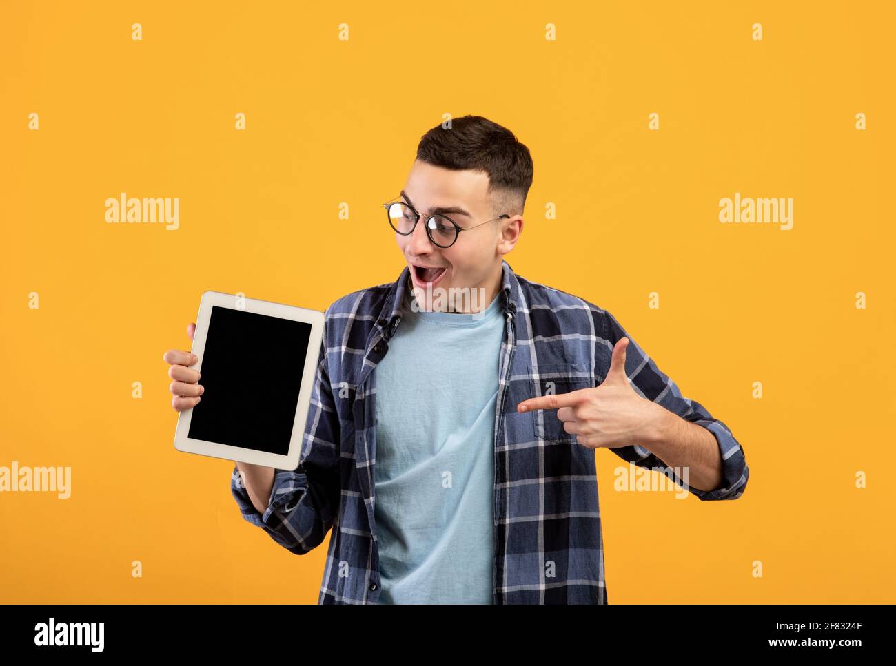 Un jeune homme joyeux qui pointe vers un Tablet pc avec une maquette pour conception de sites web ou d'applications sur fond orange studio Banque D'Images