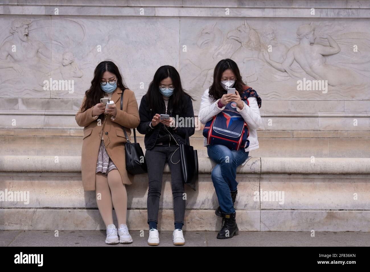 Le jour de l'annonce de la mort du duc d'Édimbourg, trois visiteurs asiatiques au pied du Victoria Memorial, en face du palais de Buckingham, s'arrêtent pour vérifier et envoyer des messages sur leur téléphone, le 9 avril 2021, à Londres, en Angleterre. Banque D'Images