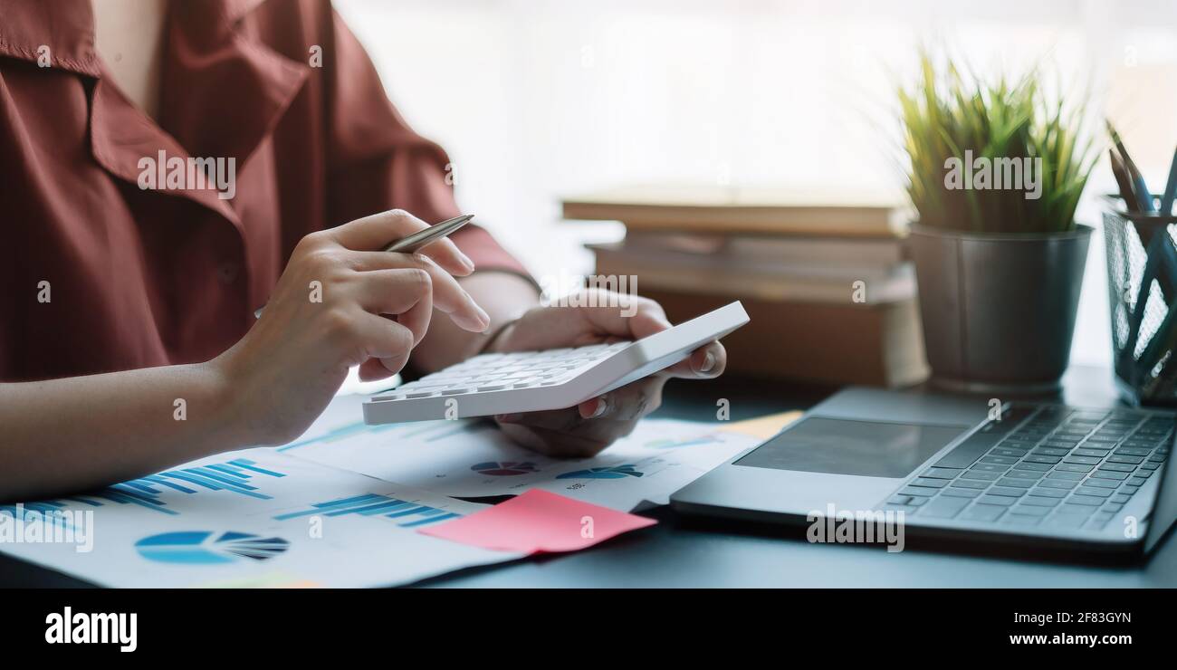 Femme d'affaires utilisant la calculatrice pour faire des finances mathématiques sur le bureau en bois dans le bureau, la taxe, la comptabilité, les statistiques maison comptable concept. Banque D'Images
