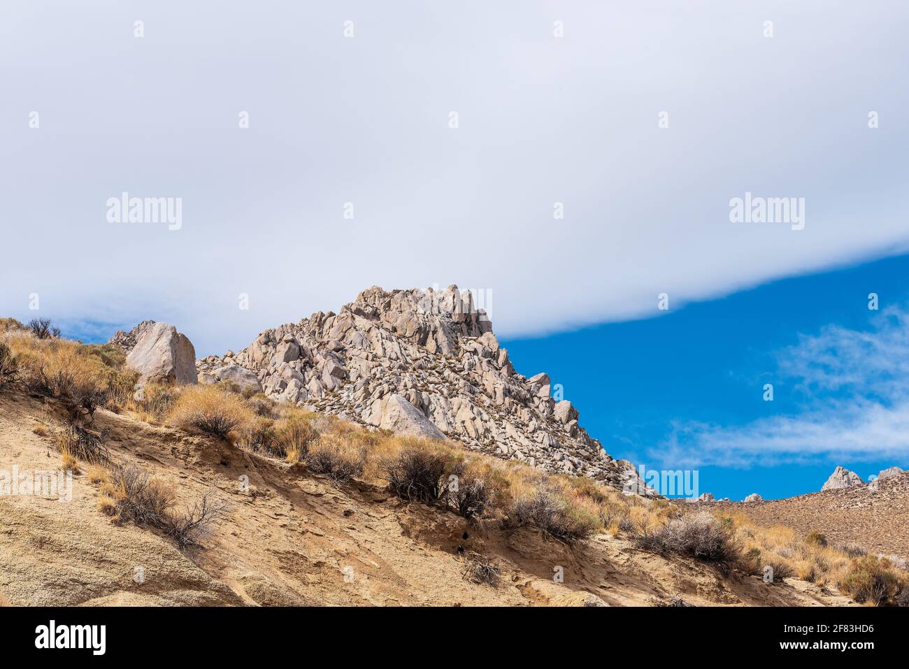 Vue depuis une colline marron escarpée au sommet rocheux sous un ciel bleu avec des nuages blancs. Banque D'Images