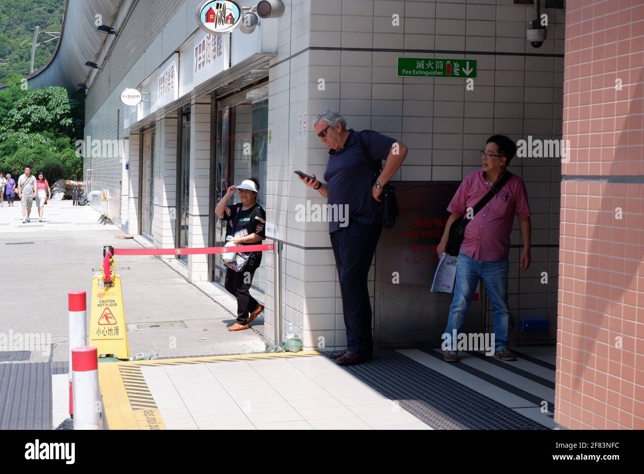 Une paire de vieux hommes attendant sous l'ombre à Sortie de la station MTR à Shek Mun Hong Kong Banque D'Images