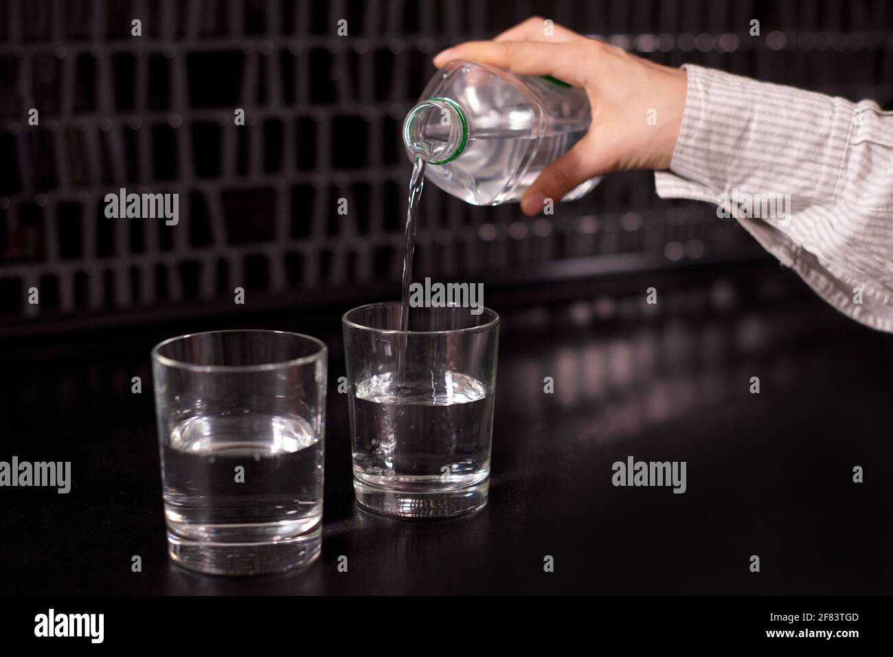 fille versant de l'eau dans un verre. deux verres avec de l'eau versant de l'eau propre sur une table noire Banque D'Images