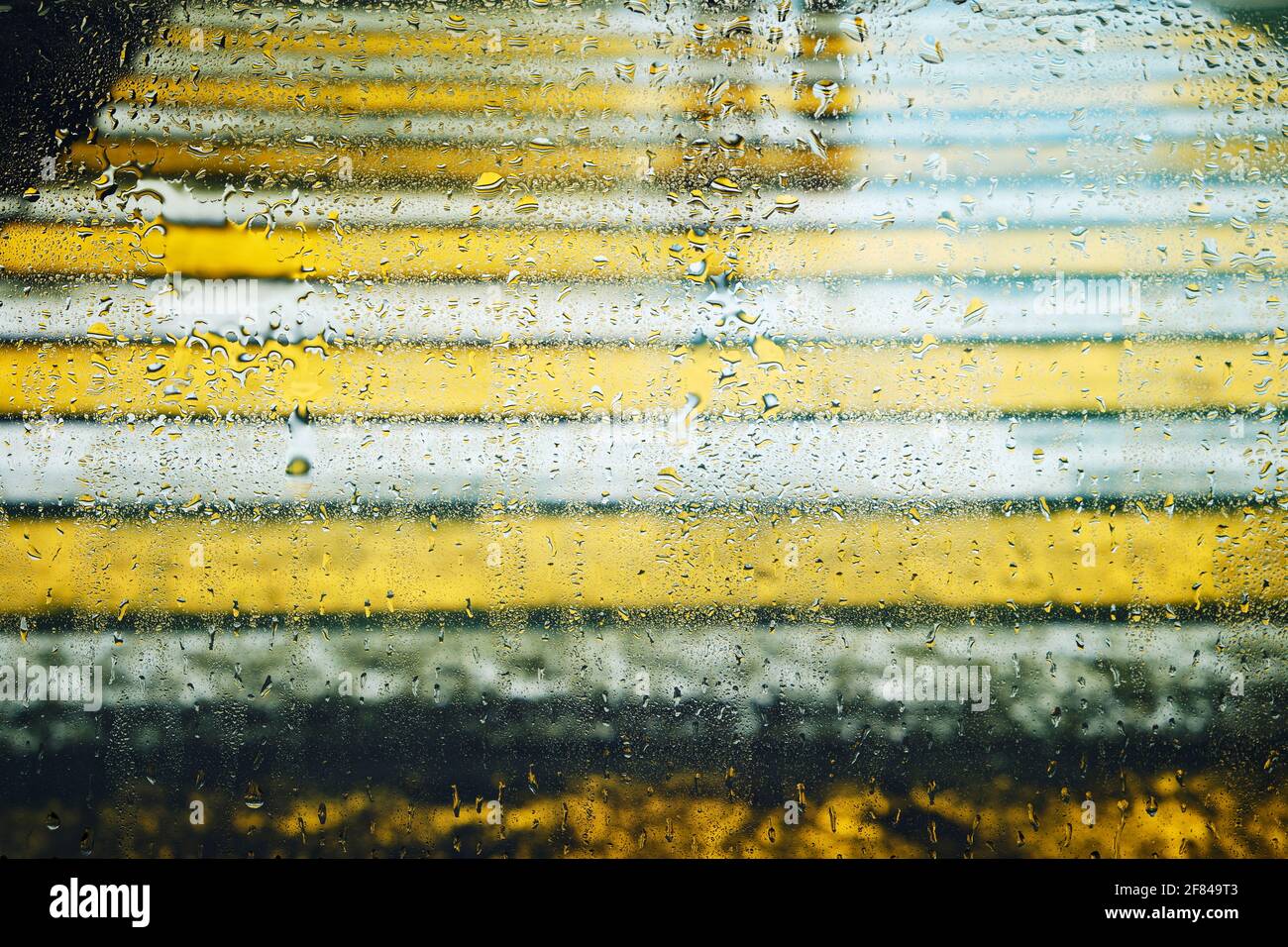 Mouiller le verre dans les gouttes de pluie sur le fond flou de la traversée pour piétons avec le reflet des personnes marchant Banque D'Images