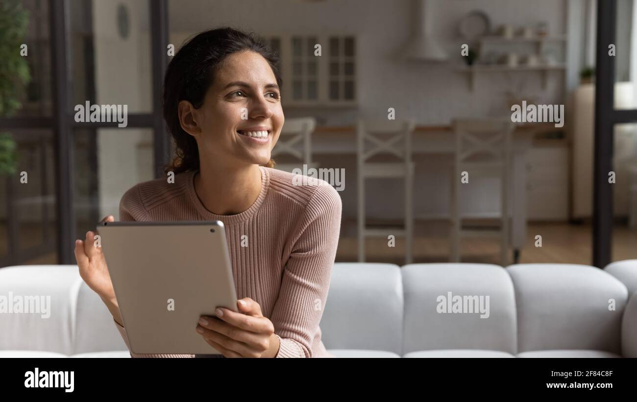 Une femme latine rêveuse travaille sur tablette en ligne regarder la distance Banque D'Images
