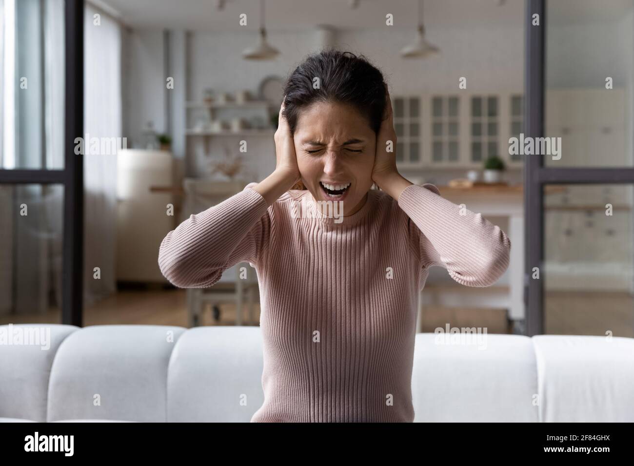 Frustrée femme hispanique millénaire devenir folle écouter le bruit dérangeant à l'intérieur Banque D'Images