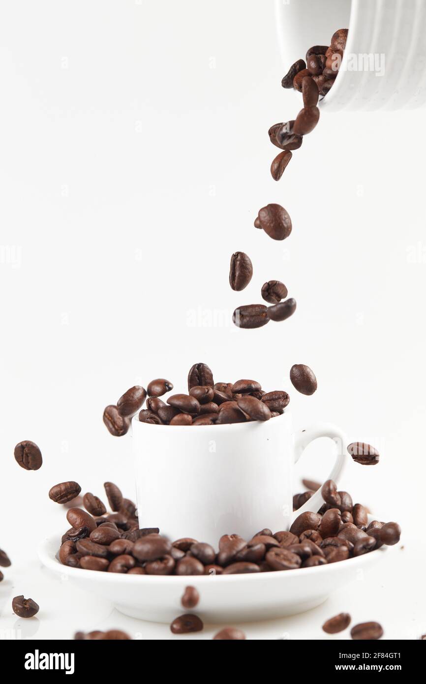 grains de café tombant dans une tasse de café isolés sur fond blanc Banque D'Images