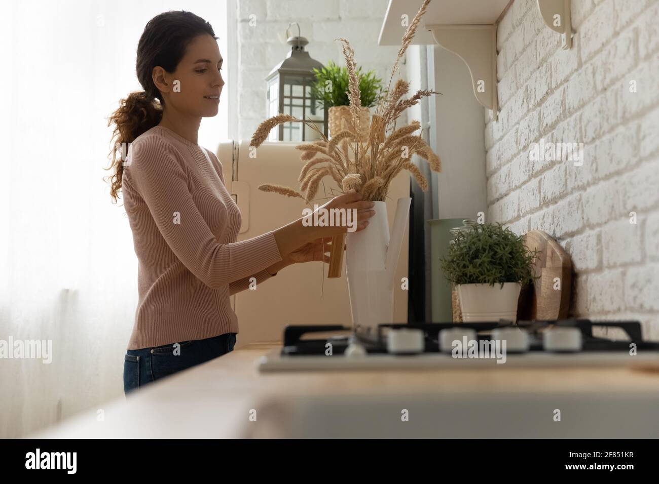 La propriétaire d'une maison organise le bouquet de plantes sèches au comptoir de la cuisine Banque D'Images