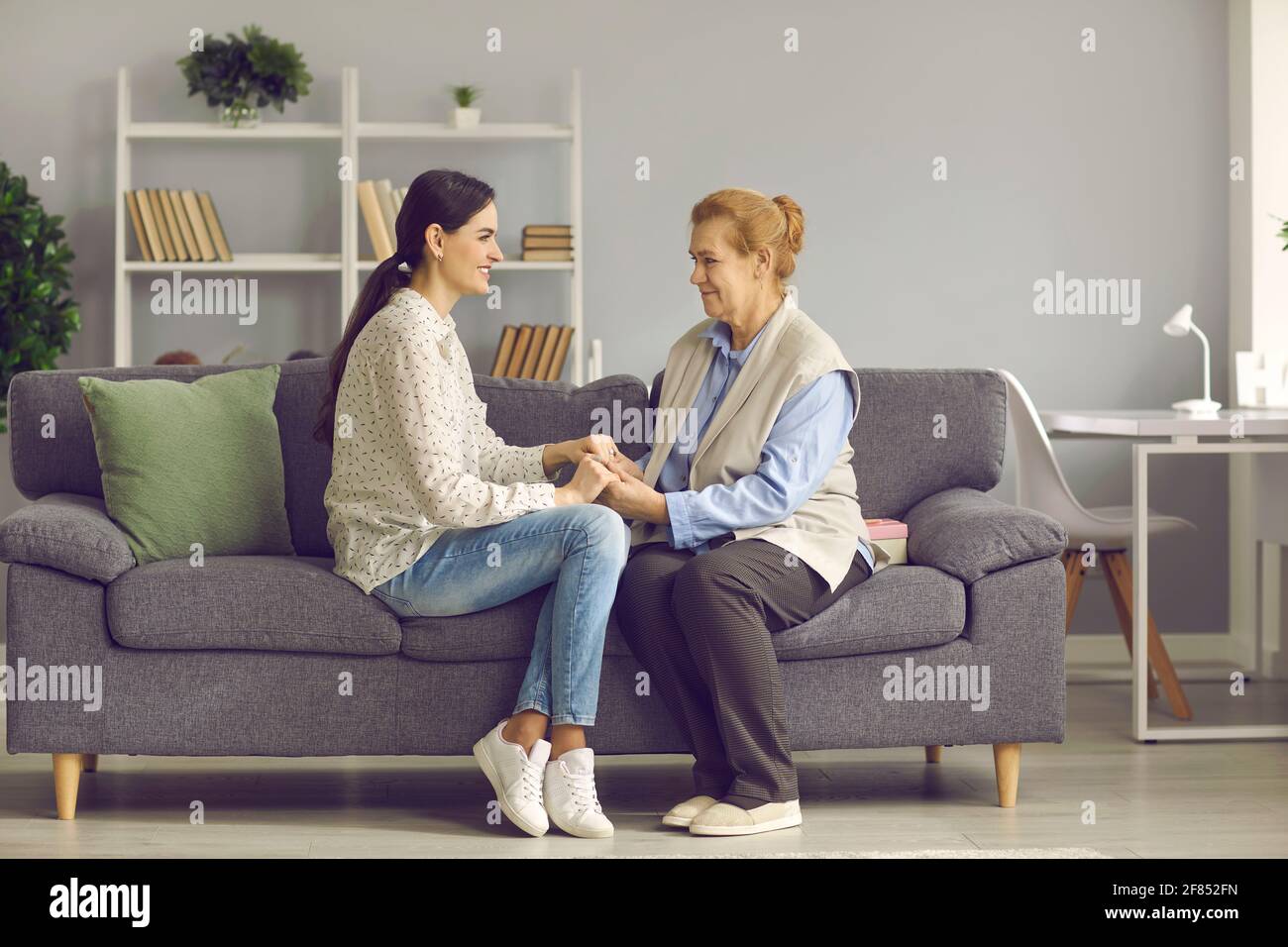 Une jeune fille et une vieille mère âgées tiennent les mains assises sur le canapé de la maison Banque D'Images