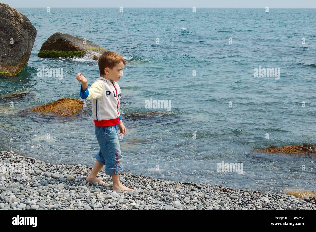 Yalta, Ukraine - 03.05.2009: Un garçon court le long de la mer. Les enfants adorent jouer avec les rochers sur la plage de galets. Banque D'Images