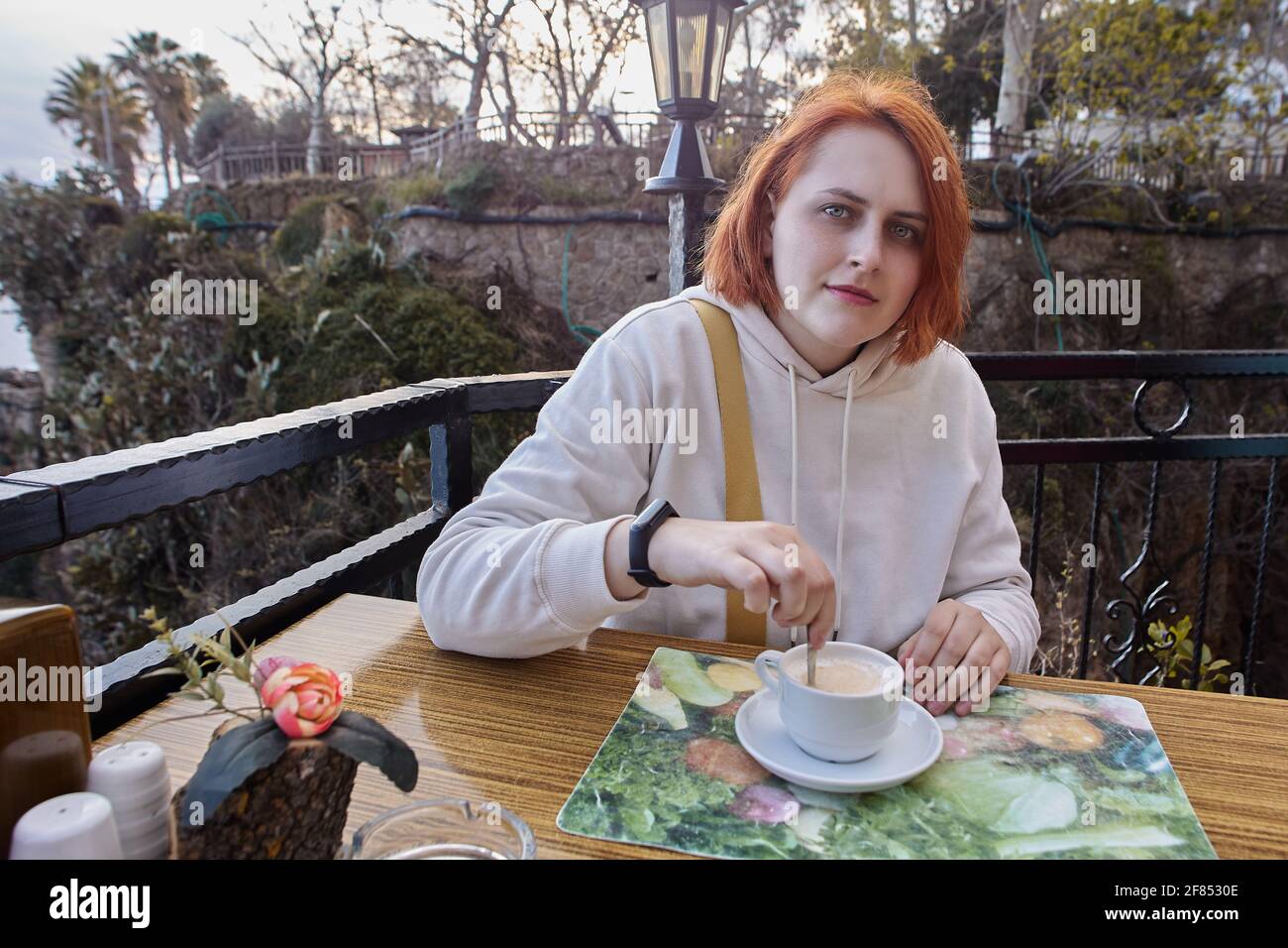 Terrasse de restaurant en bord de mer à Antalya, Turquie, jeune femme européenne aux cheveux rouges se détendant à table avec une tasse de café. Banque D'Images