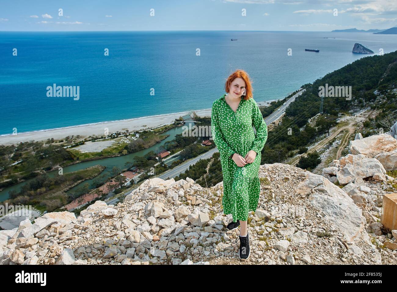 Jeune femme européenne en robe d'été verte pose pour photographe sur le rocher au-dessus de la mer au début du printemps Antalya, Turquie. Banque D'Images