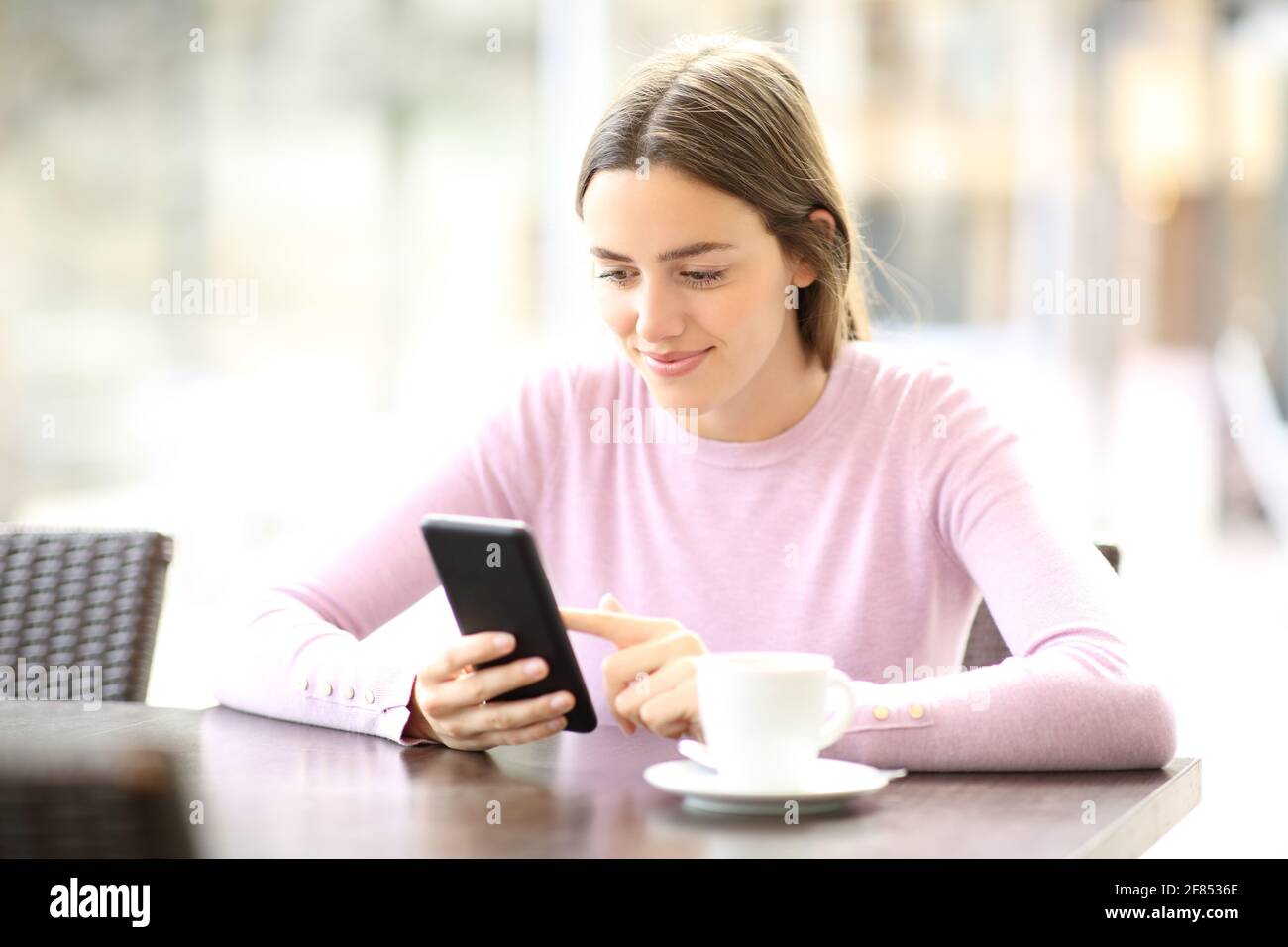 Femme satisfaite utilisant un smartphone assis dans un café une journée ensoleillée Banque D'Images