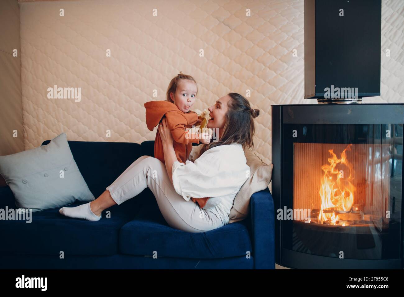 Mère et enfant assis et jouant sur un canapé près du foyer. Maman et bébé. Parent et petit enfant se détendant à la maison. Famille s'amuser ensemble Banque D'Images