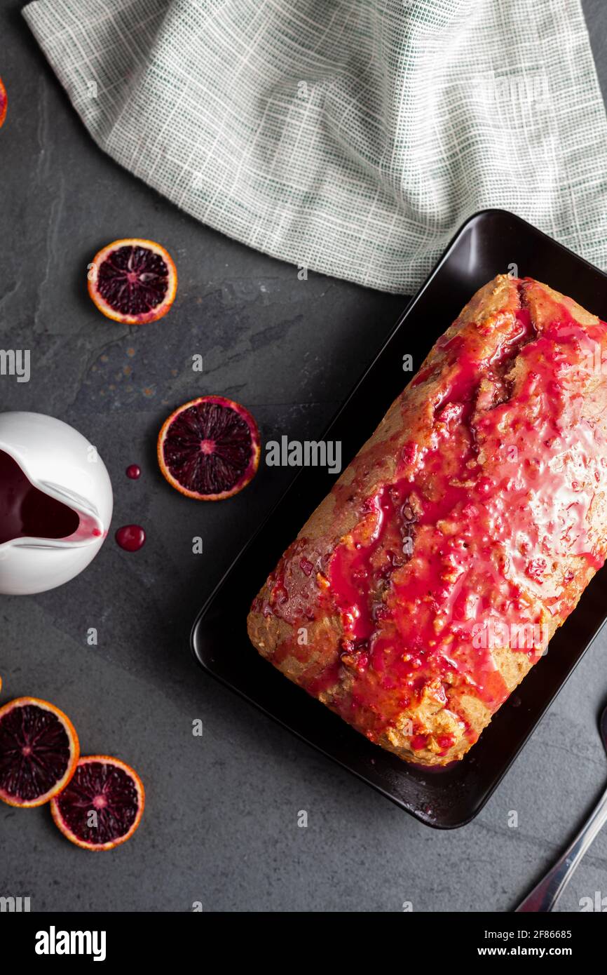 Image en gros plan d'un gâteau d'orange de sang frais fait maison dans un moule à pain et servi sur une assiette en porcelaine noire sur fond de pierre sombre. Il a l'orang de sang Banque D'Images