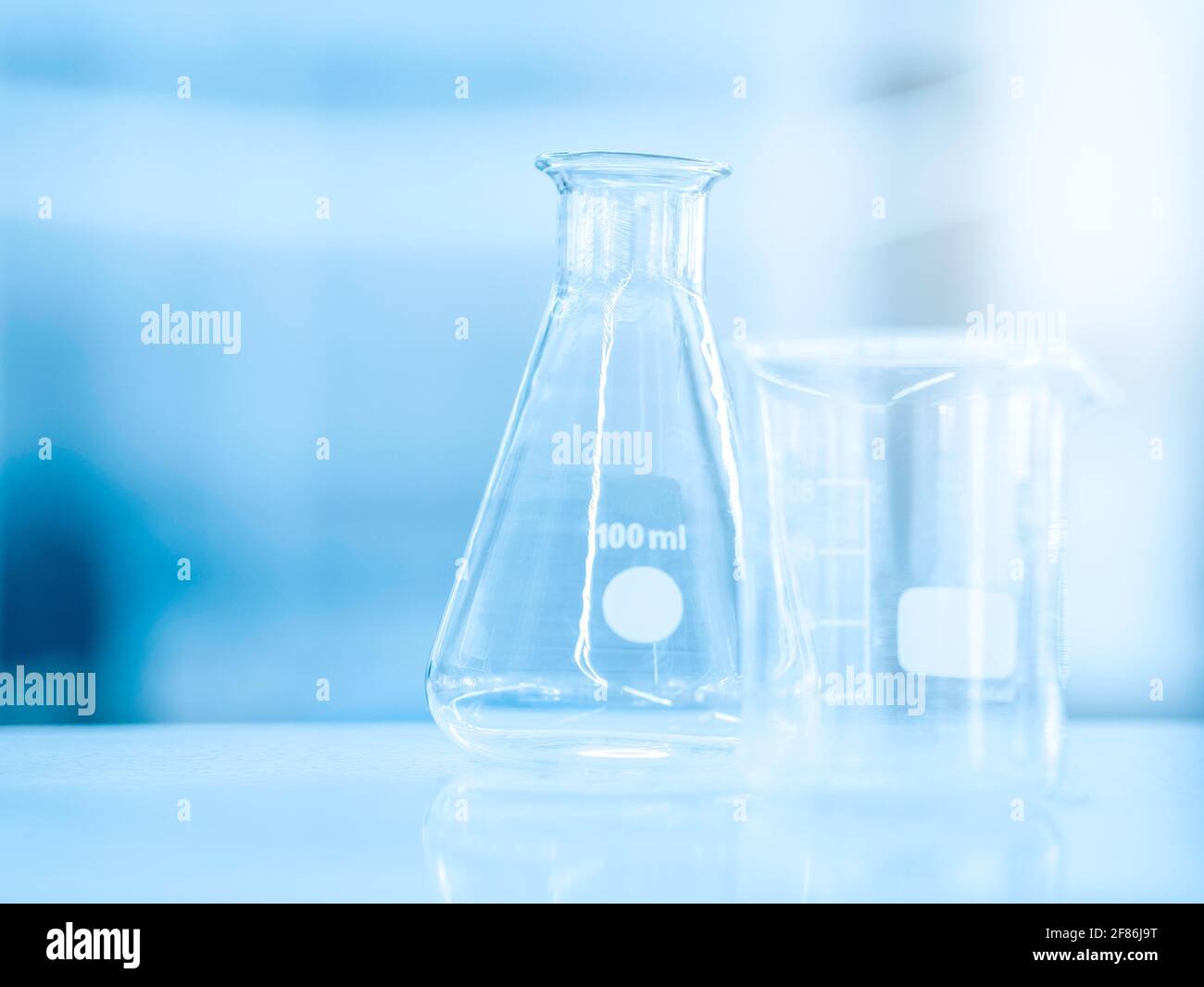 Flacon en verre vide de 100 ml et bécher de mesure en laboratoire de chimie bleue pour une expérience scientifique avec un espace de copie. Équis. Scientifique Banque D'Images