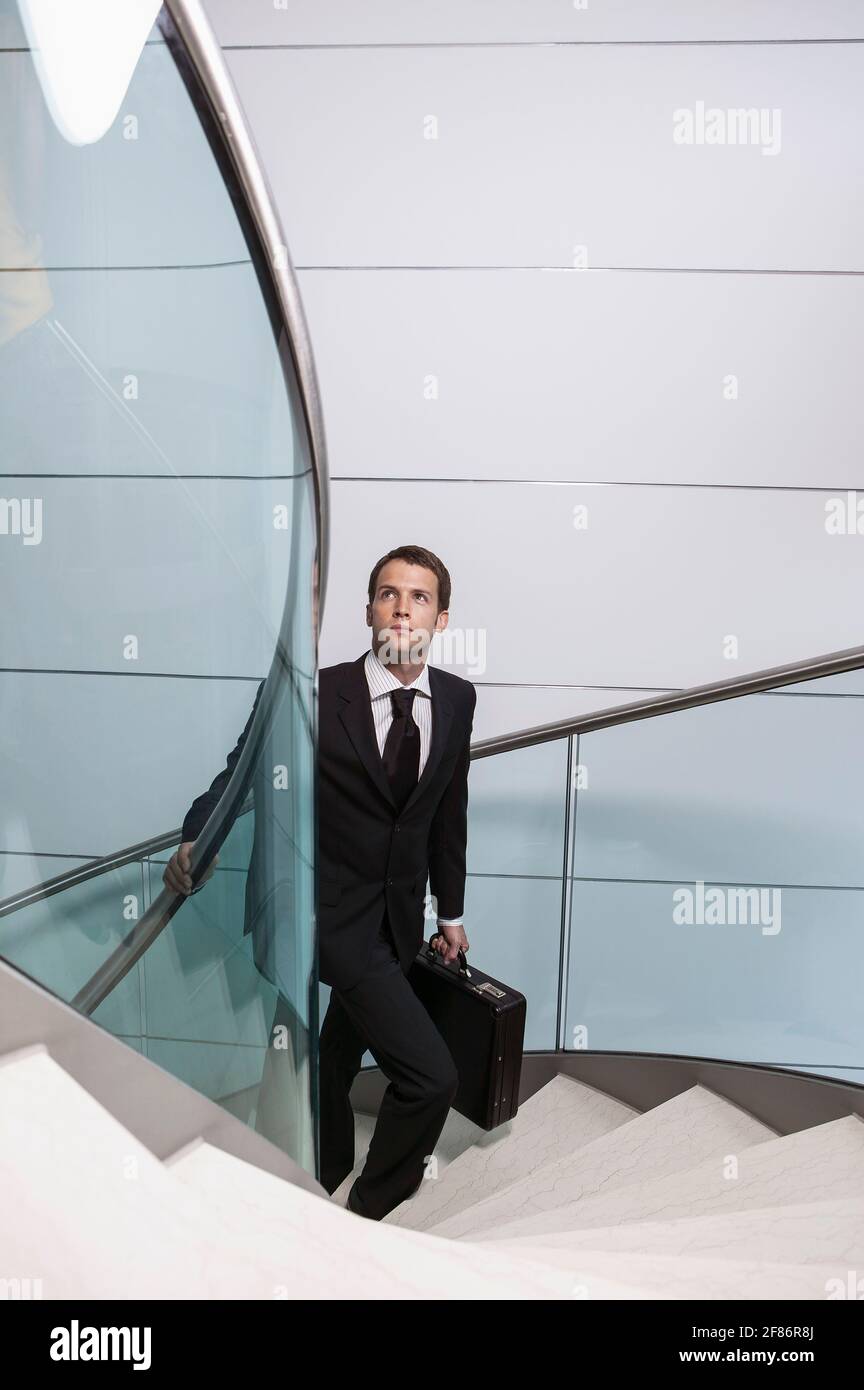 Homme d'affaires avec porte-documents donnant sur l'escalier en colimaçon ascendant Banque D'Images