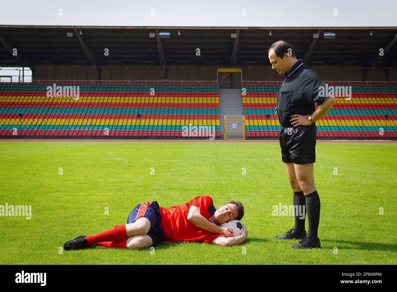 Entraîneur de football regardant le joueur dormir sur le terrain ensoleillé Banque D'Images