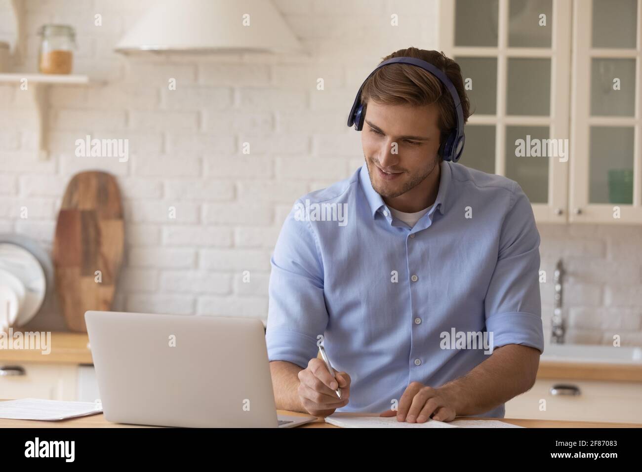 Homme motivé dans le casque, regardant un webinaire, prenant des notes, utilisant un ordinateur portable Banque D'Images