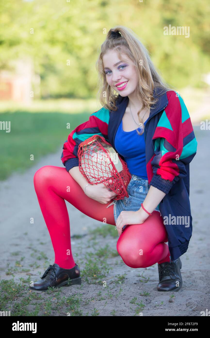 Une belle fille de campagne des années 90 en vêtements brillants tient un  sac à ficelle avec une boîte de sève de bouleau. Femme russe dans le style  des années 90 Photo