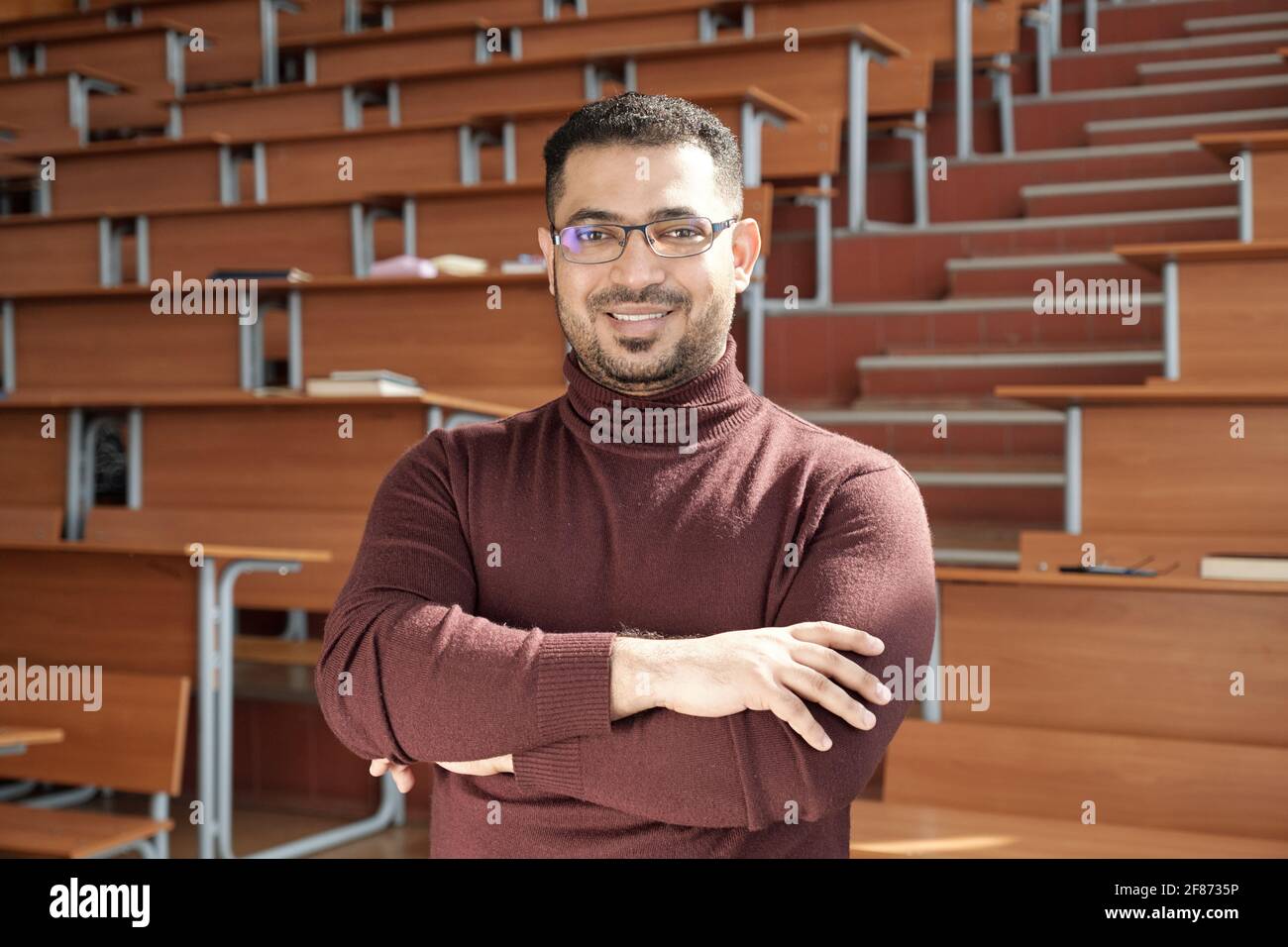 Jeune homme réussi enseignant de l'université traversant ses bras en vous tenant devant la caméra, contre les bureaux salle de conférence Banque D'Images