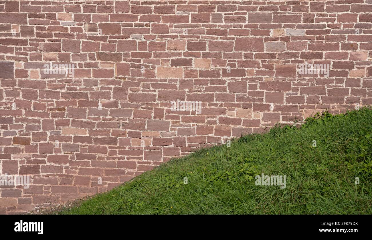 Vieux mur en grès rouge derrière une colline d'herbe Banque D'Images