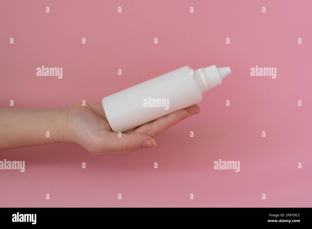 Bouteille de solution dans la main d'une femme sur fond rose Banque D'Images