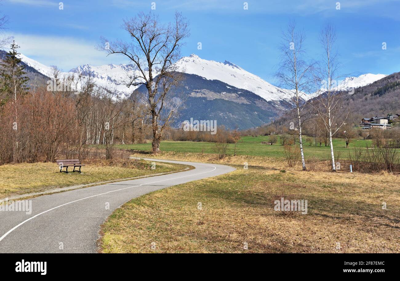 voie asphaltée avec courbe d'une voie verte traversant un vallée alpine avec fond de montagne enneigé Banque D'Images