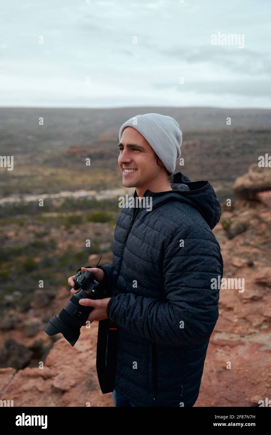 Photographe masculin tenant un appareil photo reflex numérique à la main à la recherche du photo parfaite en montagne en hiver Banque D'Images