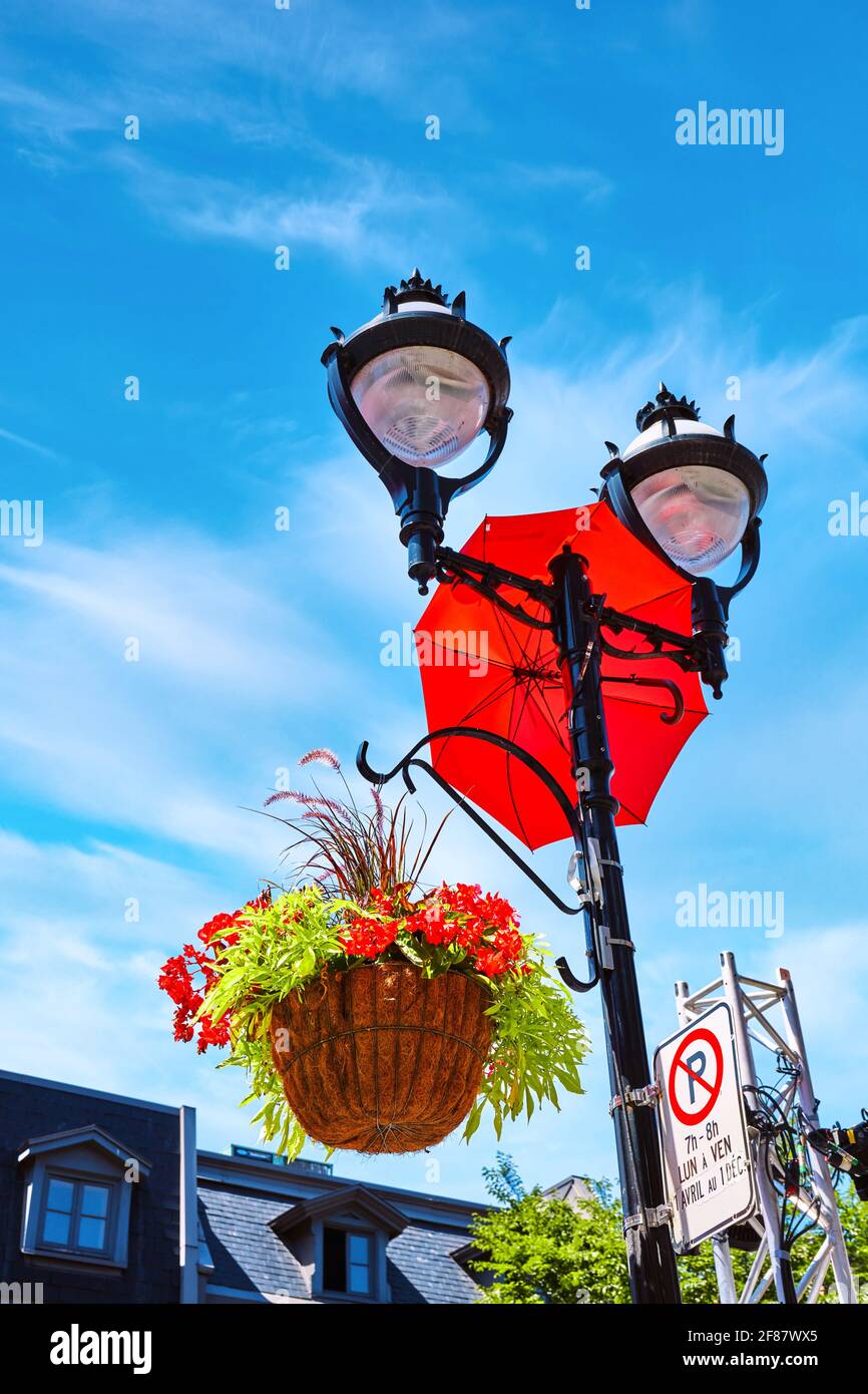 Pétunias rouges dans un panier de fleurs accroché à un poteau lumineux de rue avec un parapluie rouge décoratif. Décoration et ornements de ville. Banque D'Images