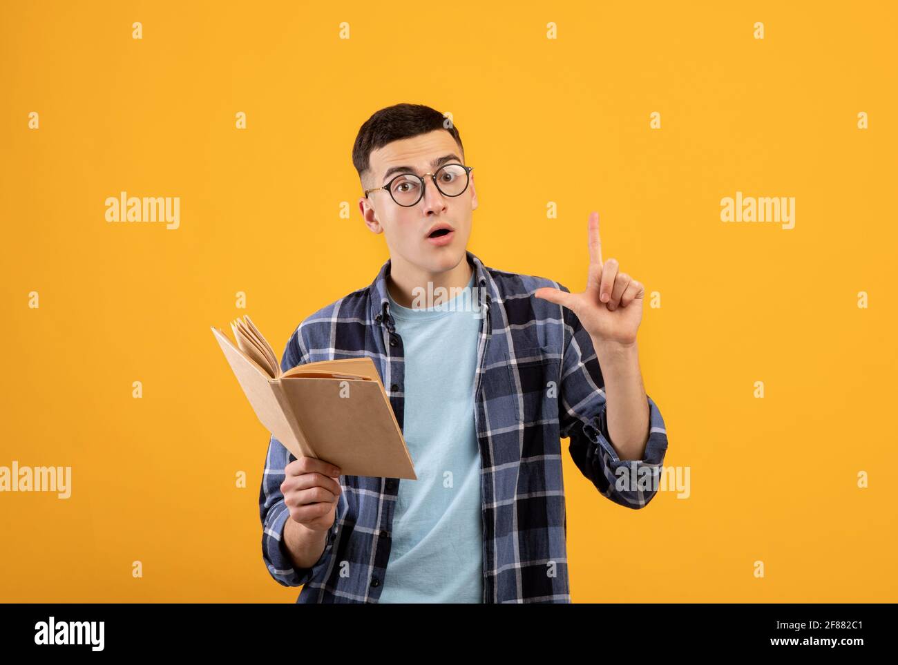 Jeune homme intelligent avec un livre montrant son intelligence, en faisant le geste d'eureka, ayant une idée créative sur fond orange Banque D'Images