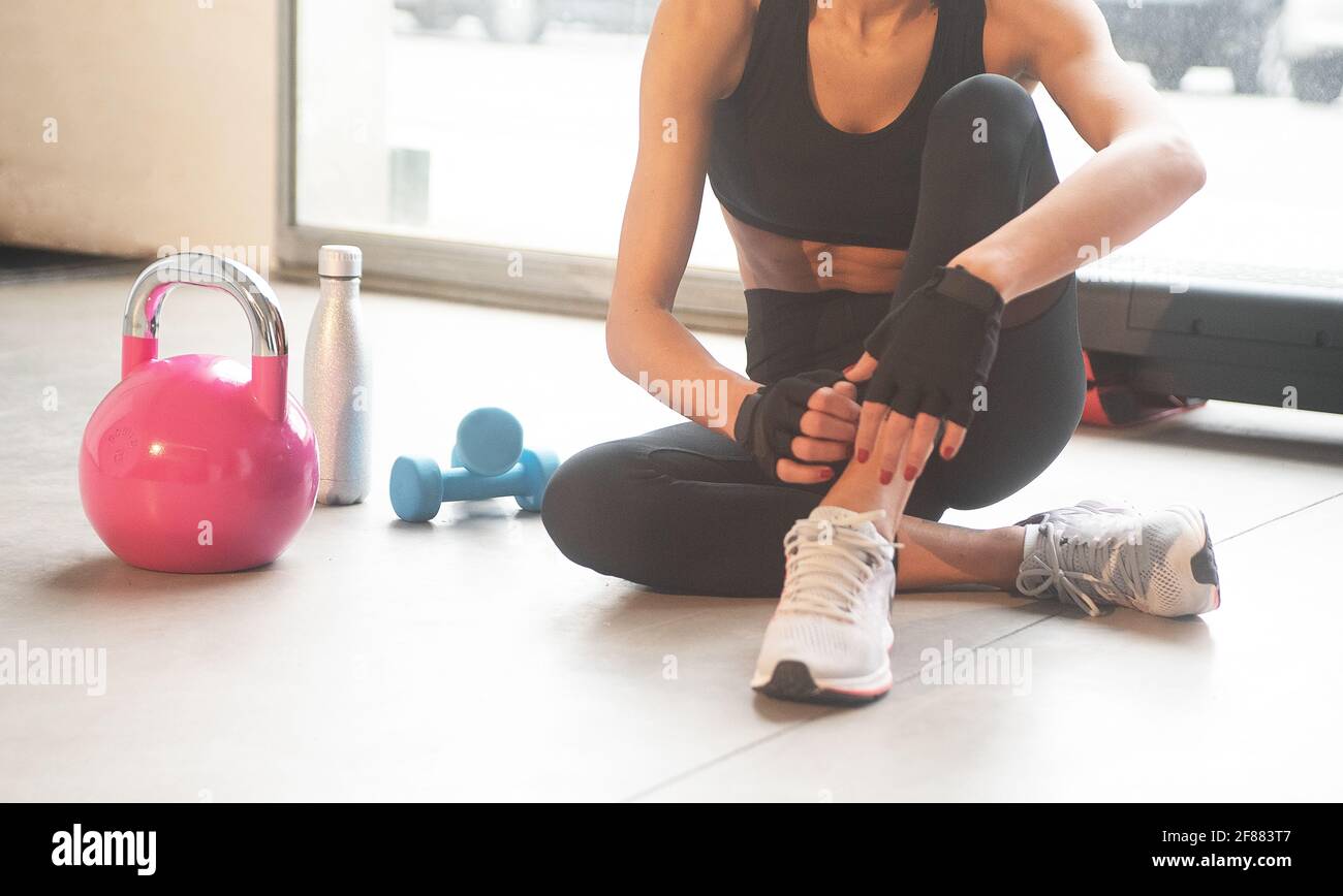 Gros plan d'une haltère bleu clair sur le sol d'une salle de gym avec une kettlebell rose une bouteille d'argent d'eau et une jeune femme assise à l'horizontale Banque D'Images