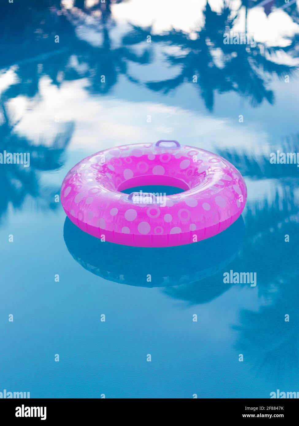 dispositif de flottaison de piscine rose dans une piscine avec des réflexions de palmiers Banque D'Images