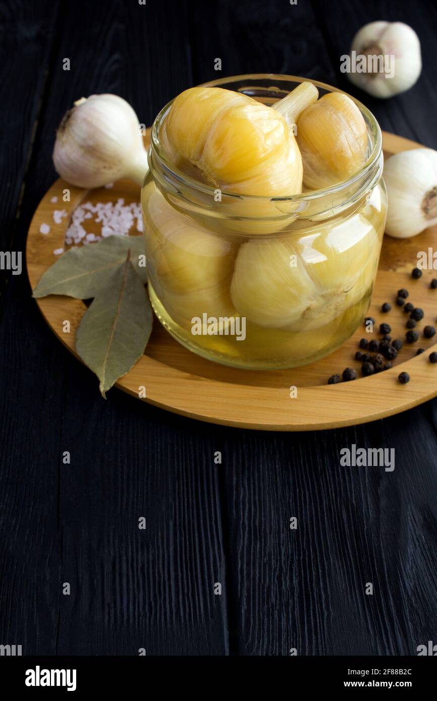 Ail mariné dans le pot en verre sur la planche à découper brune sur fond de bois noir. Produit fermenté fait maison. Banque D'Images