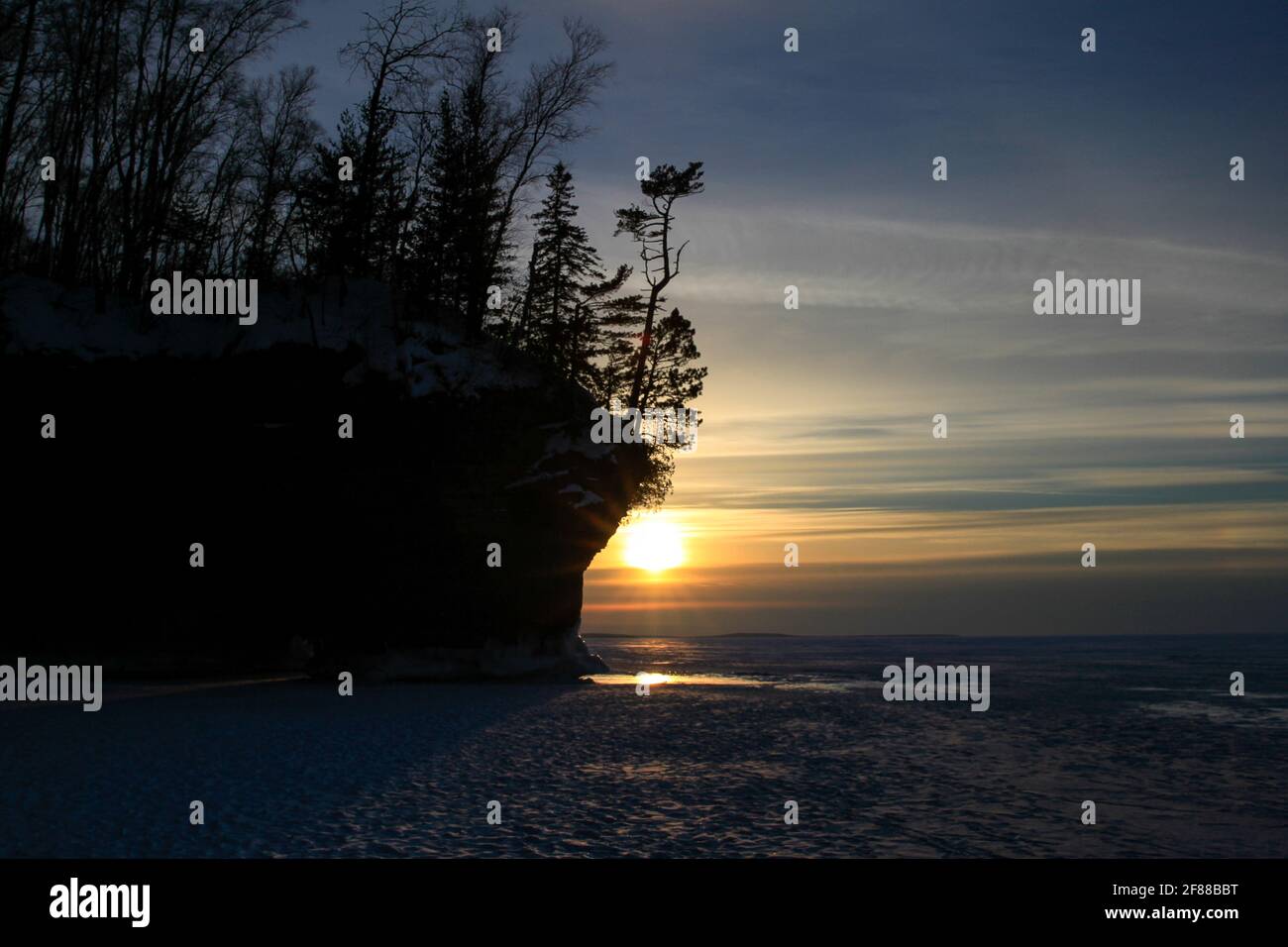 Coucher de soleil derrière la falaise au-dessus du lac supérieur gelé sur les îles Apôtre Banque D'Images