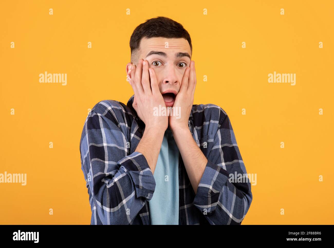 Jeune homme hippster se sentant peur, essayant de cacher son visage sur fond orange studio Banque D'Images