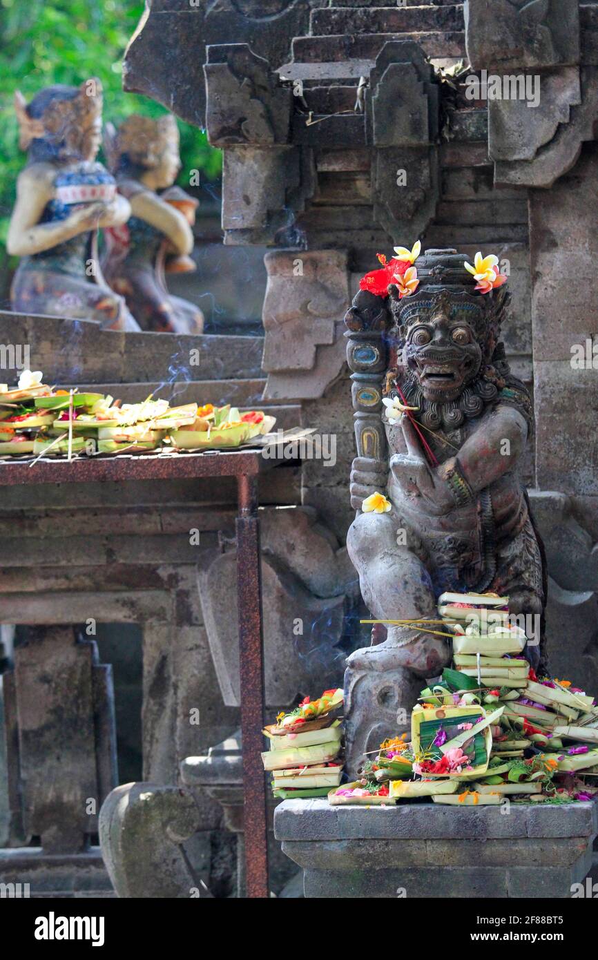 Statue traditionnelle en pierre sculptée au temple avec des fleurs et de l'encens à Bali, en Indonésie Banque D'Images