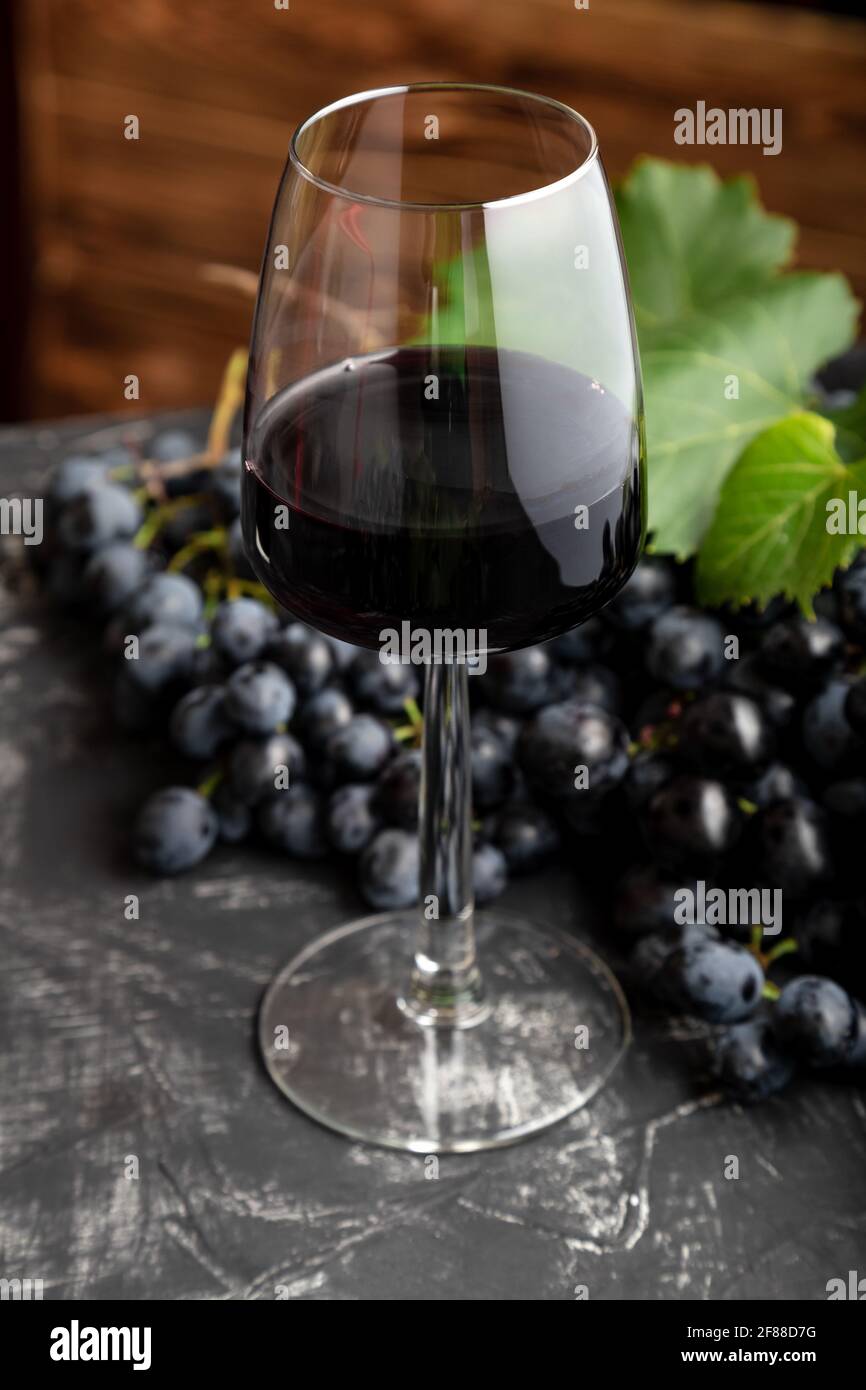 Verre à vin avec vin rouge sur table noire, fond en bois sombre. Boisson au  vin rouge en verre avec raisins noirs. Beaujolais composition du vin au  café ou à la res