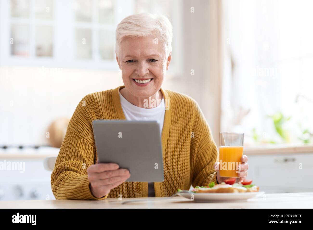 Femme âgée souriante prenant le déjeuner et utilisant une tablette numérique Banque D'Images