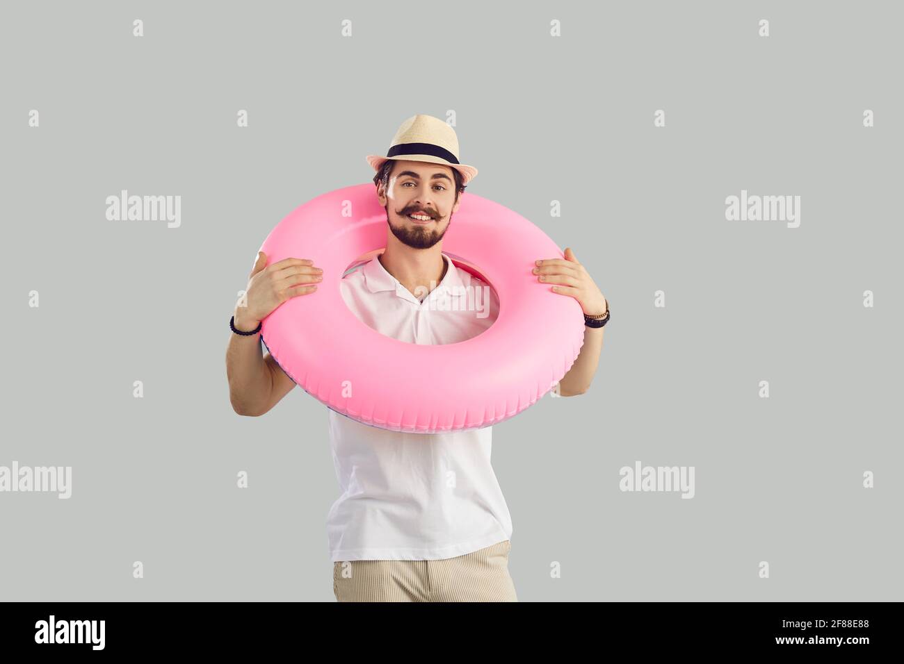 Homme avec un anneau gonflable rose en caoutchouc autour de son cou est debout sur un fond gris. Banque D'Images