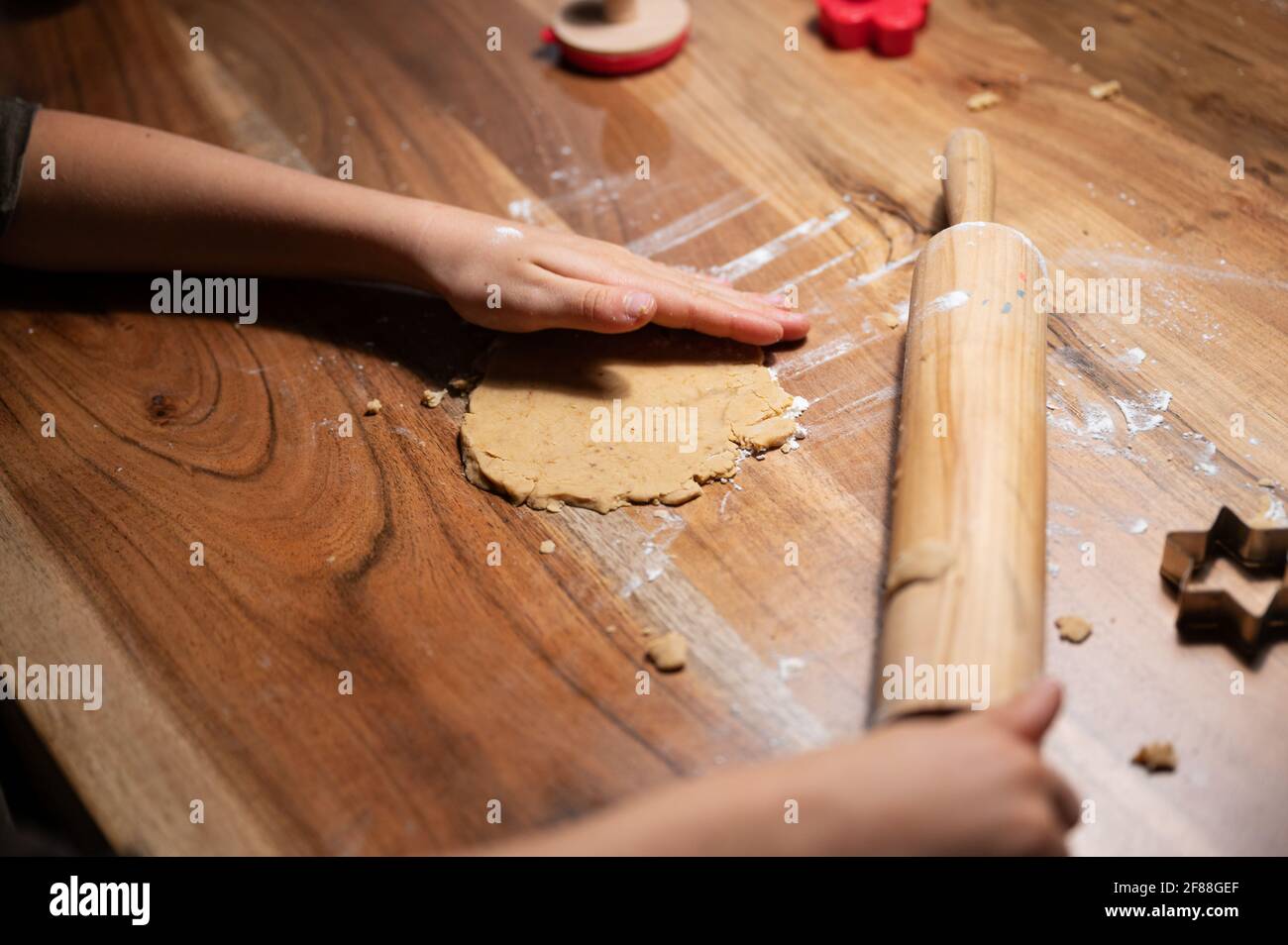 Vue en gros plan d'un enfant qui fait des biscuits faits maison roulant la pâte avec un rollpin sur une table. Banque D'Images