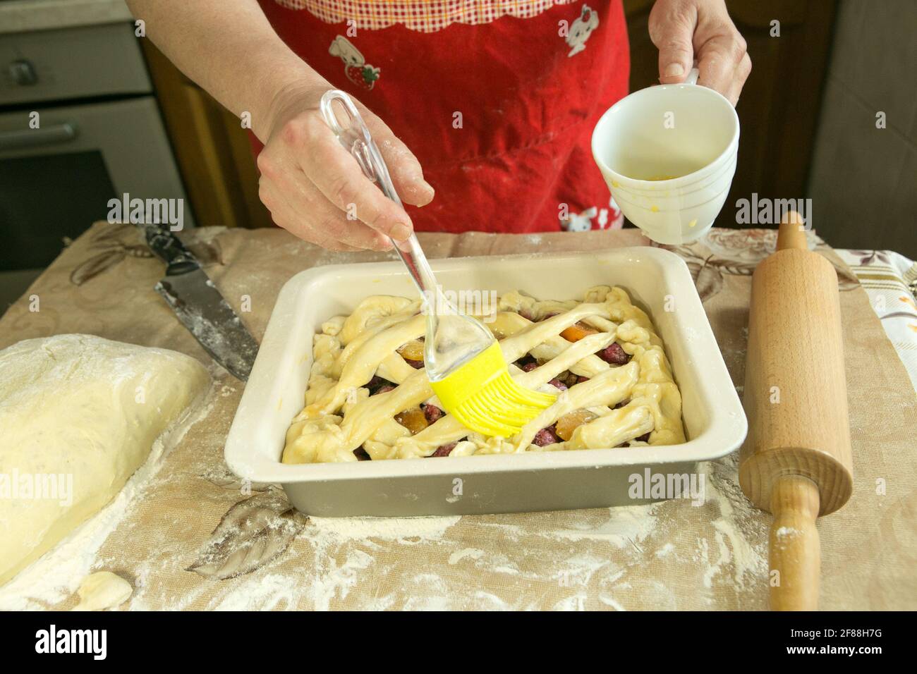 Chaussons de maman. Maman lubrifie le gâteau avant de le cuire avec une brosse de cuisson. Mains de femmes. Cuisson en quarantaine. Banque D'Images