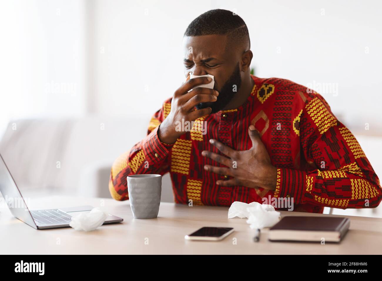 Grippe saisonnière. Un homme africain malade en vêtements tribaux se sent mal au travail Banque D'Images